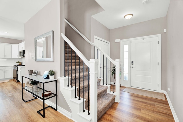 entryway with stairway, light wood finished floors, and baseboards