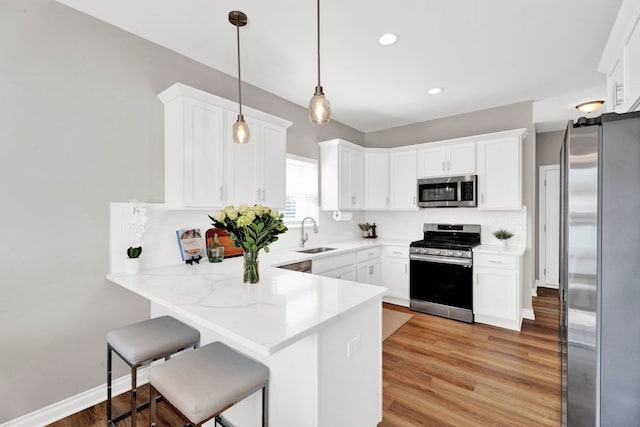 kitchen with a peninsula, white cabinetry, appliances with stainless steel finishes, and a sink