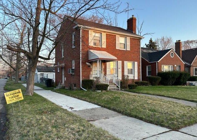 colonial home with brick siding, a chimney, and a front lawn