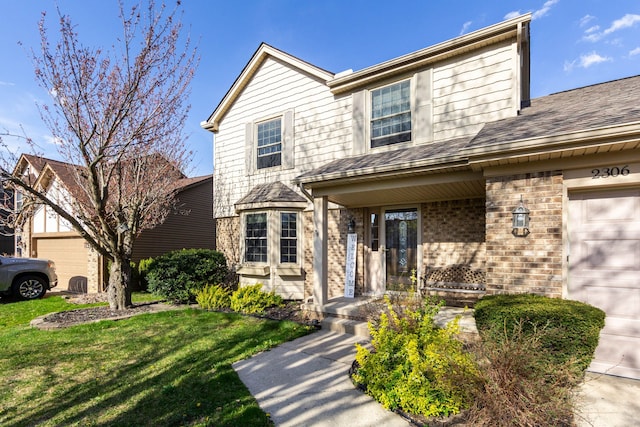 traditional home with roof with shingles, brick siding, a garage, a front yard, and covered porch
