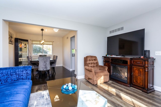 living room with visible vents, baseboards, a glass covered fireplace, and wood finished floors