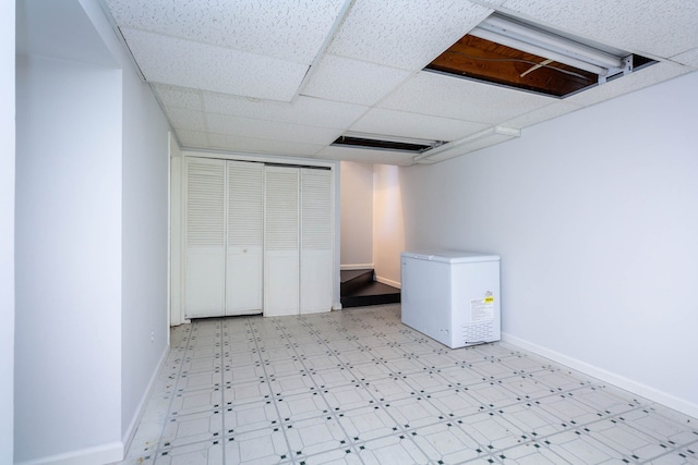 finished below grade area with light floors, baseboards, a drop ceiling, and refrigerator