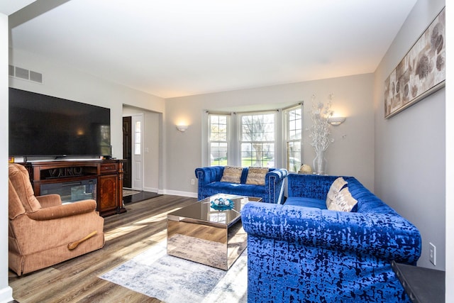 living room with a glass covered fireplace, baseboards, wood finished floors, and visible vents