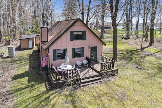 rear view of house with a chimney, a lawn, a deck, a storage shed, and an outbuilding