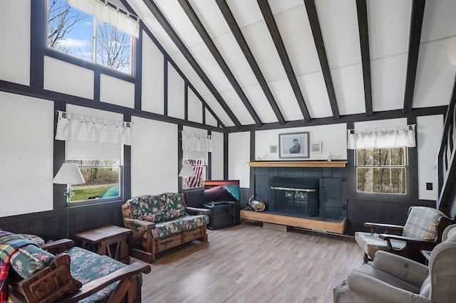 living area featuring high vaulted ceiling, beam ceiling, a brick fireplace, and wood finished floors
