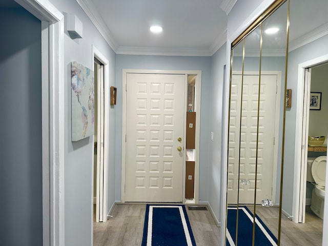 entryway with baseboards, crown molding, and light wood-style flooring