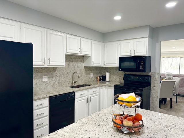 kitchen featuring black appliances, a sink, white cabinets, and light stone counters