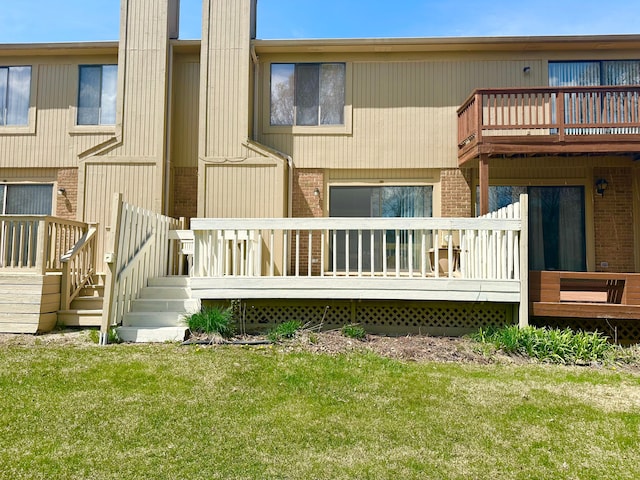 rear view of house with a lawn, a deck, and brick siding