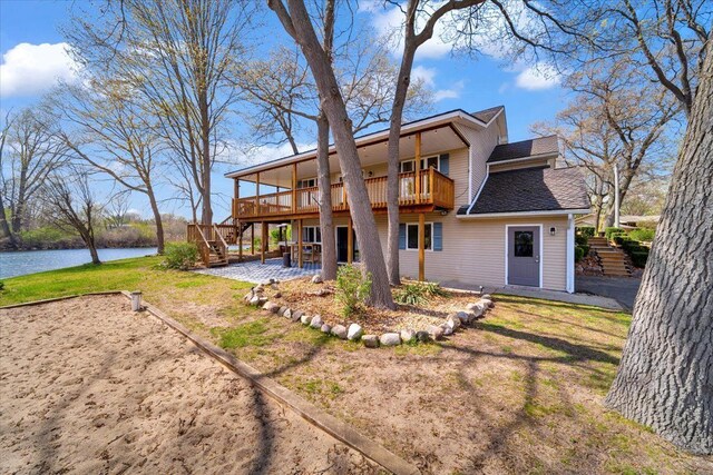 back of house with a deck with water view, a patio, stairs, a shingled roof, and a lawn
