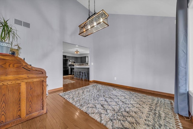 interior space with visible vents, baseboards, wood finished floors, and high vaulted ceiling
