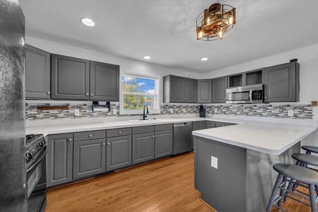 kitchen featuring gray cabinets, a kitchen breakfast bar, a sink, black appliances, and light wood-style floors