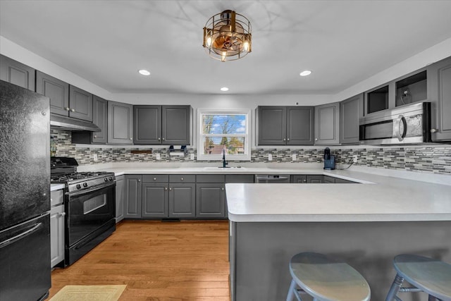 kitchen with a sink, a peninsula, under cabinet range hood, gray cabinetry, and black appliances