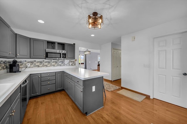 kitchen with open shelves, gray cabinets, a peninsula, stainless steel microwave, and backsplash