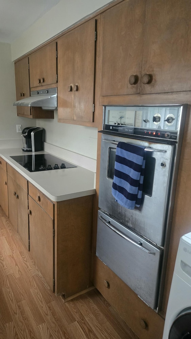kitchen with a warming drawer, under cabinet range hood, oven, black electric cooktop, and washer / clothes dryer