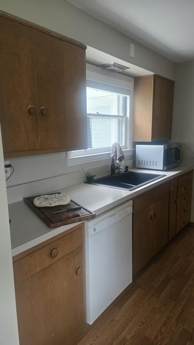 kitchen with dark wood-style flooring, dishwasher, light countertops, and a sink