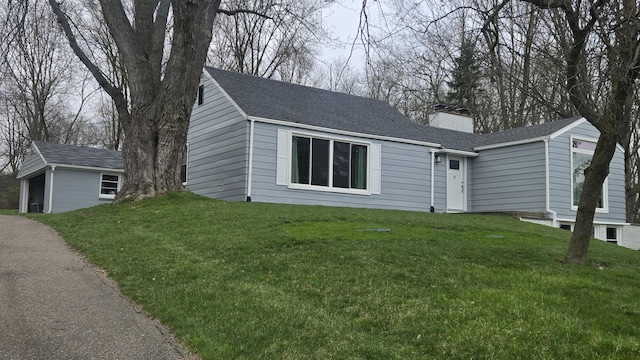 ranch-style house with roof with shingles, a chimney, a front yard, and an outbuilding