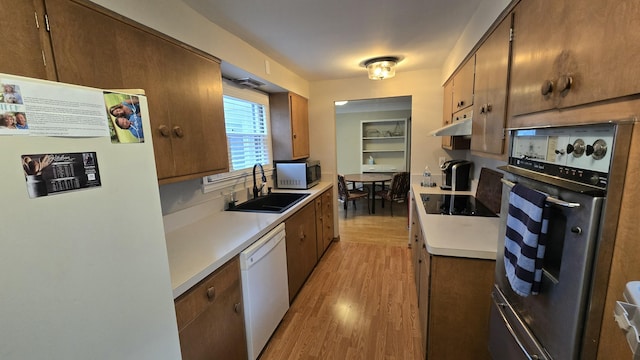 kitchen featuring a sink, under cabinet range hood, light wood-style floors, white appliances, and light countertops