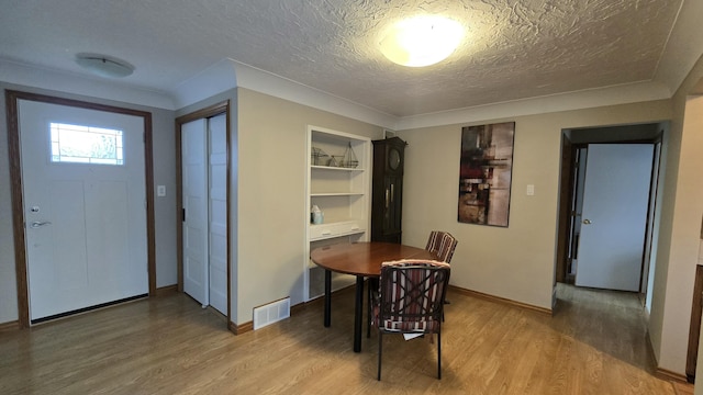 dining space with a textured ceiling, visible vents, light wood-style flooring, and baseboards