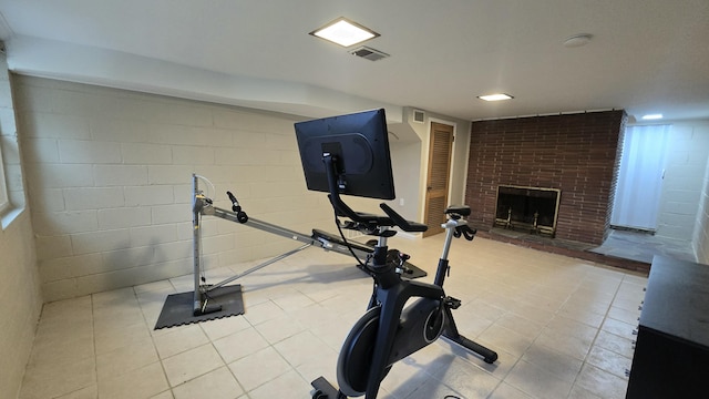 exercise area featuring light tile patterned floors, visible vents, concrete block wall, and a fireplace