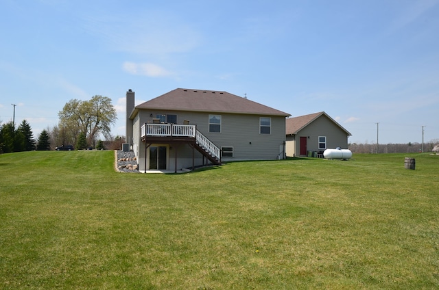 back of property featuring a chimney, stairway, a wooden deck, and a lawn