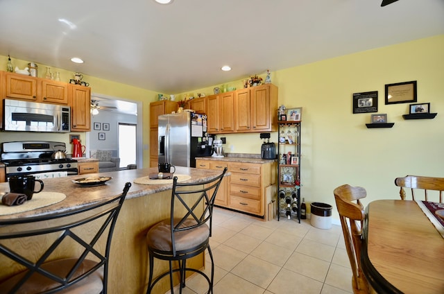 kitchen with recessed lighting, light tile patterned flooring, a kitchen breakfast bar, a ceiling fan, and appliances with stainless steel finishes