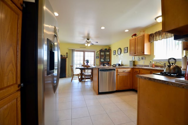 kitchen with a sink, appliances with stainless steel finishes, a peninsula, a ceiling fan, and brown cabinetry
