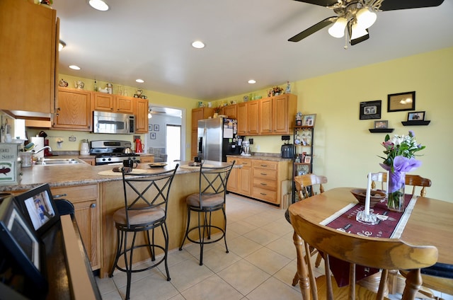 kitchen featuring light tile patterned floors, a sink, appliances with stainless steel finishes, ceiling fan, and a peninsula