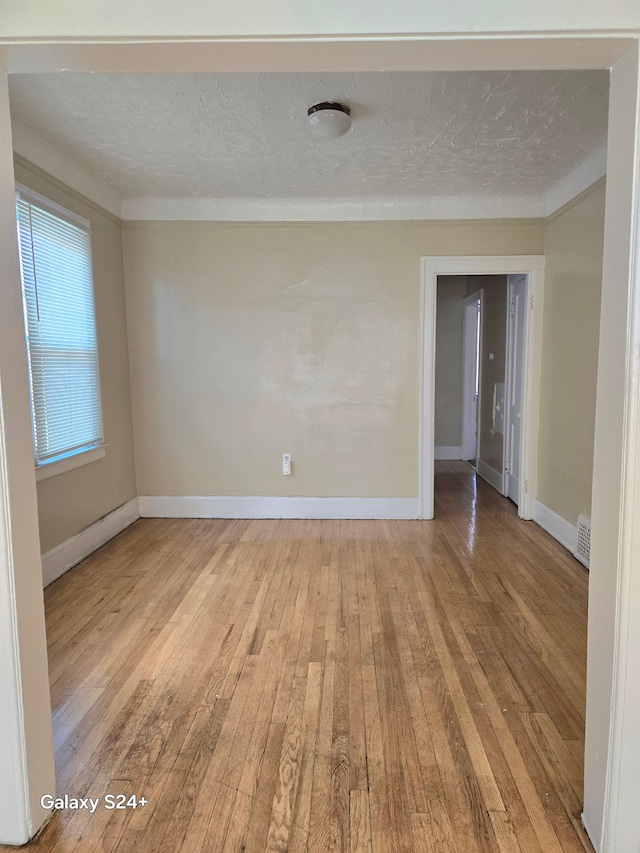 spare room with a textured ceiling, baseboards, visible vents, and hardwood / wood-style floors
