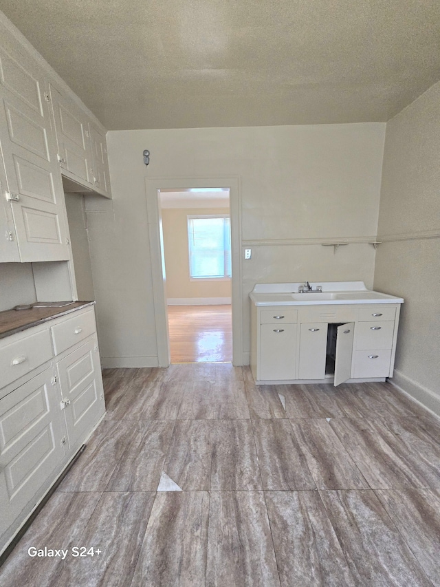kitchen with a textured ceiling, a sink, baseboards, white cabinets, and light wood-style flooring