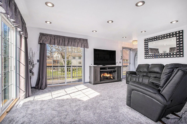 carpeted living area with a warm lit fireplace, recessed lighting, and a healthy amount of sunlight
