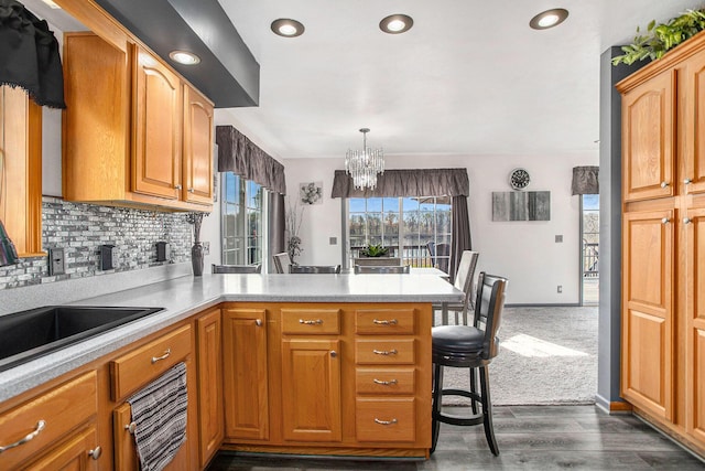 kitchen with a sink, light countertops, a peninsula, a notable chandelier, and backsplash