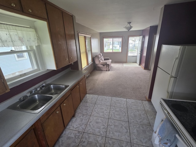 kitchen with a sink, light colored carpet, open floor plan, light tile patterned flooring, and white appliances
