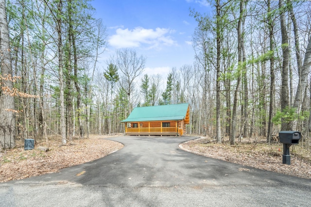 exterior space with a porch, metal roof, a wooded view, and aphalt driveway