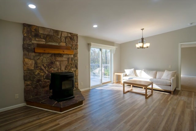 living area with wood finished floors, a chandelier, a wood stove, and baseboards
