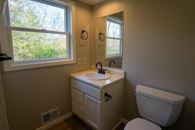 half bath featuring visible vents, toilet, vanity, and baseboards