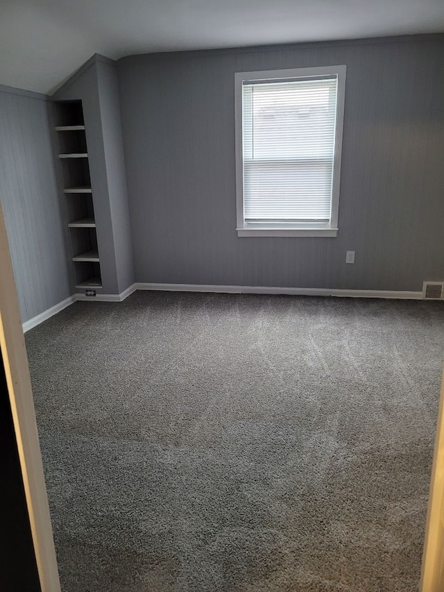 empty room featuring visible vents, carpet flooring, built in features, and baseboards