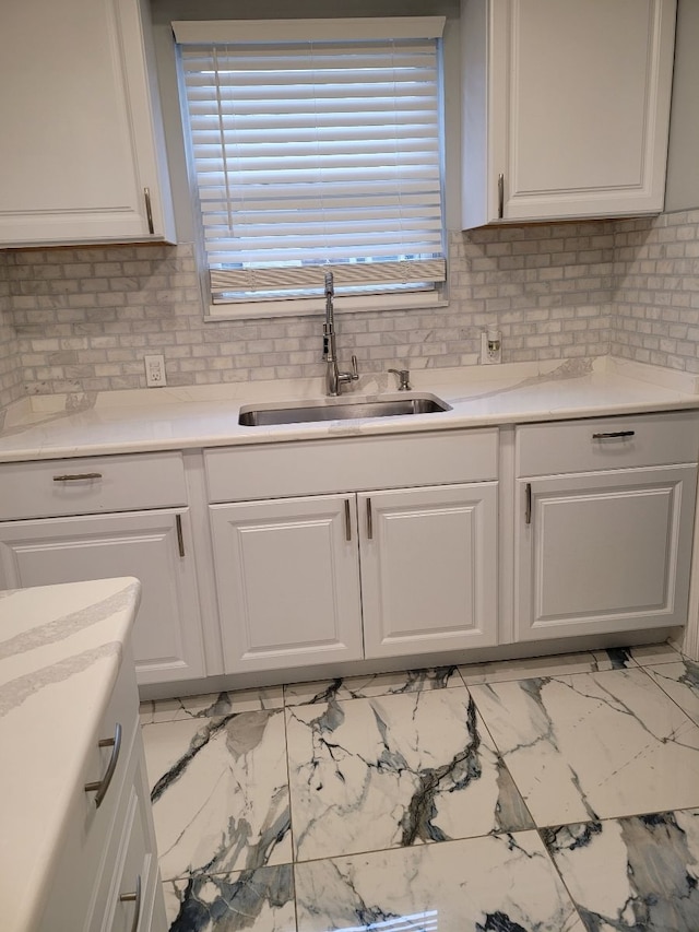 kitchen featuring white cabinetry, decorative backsplash, a sink, light countertops, and marble finish floor