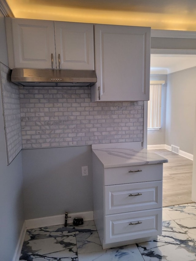 kitchen featuring baseboards, light stone countertops, under cabinet range hood, and white cabinets
