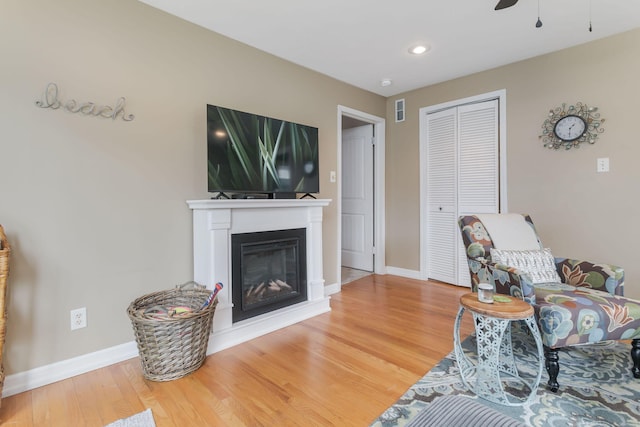 living area with wood finished floors, a ceiling fan, visible vents, and baseboards