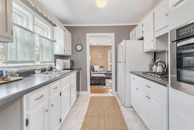 kitchen featuring dark countertops, stainless steel appliances, white cabinetry, and a sink