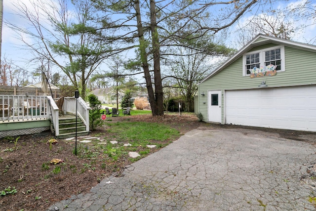 view of yard with a garage, a wooden deck, and aphalt driveway