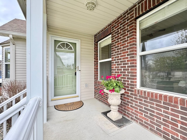 property entrance featuring covered porch, a shingled roof, and brick siding