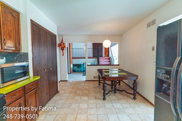 kitchen with decorative light fixtures, stainless steel microwave, decorative backsplash, refrigerator with ice dispenser, and visible vents