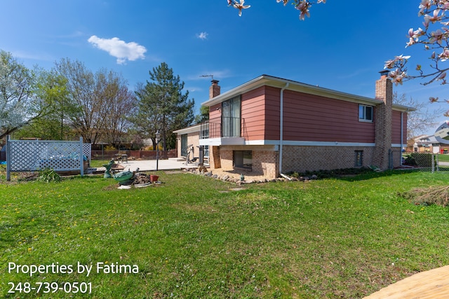 view of side of home featuring fence, a chimney, brick siding, a patio area, and a lawn