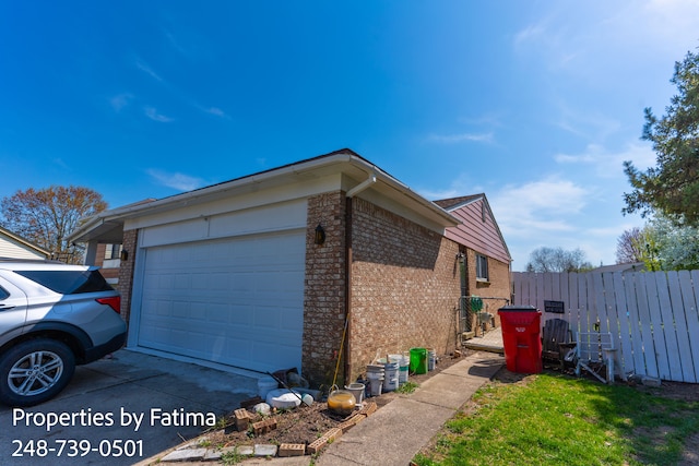 view of home's exterior with brick siding, an attached garage, fence, and concrete driveway