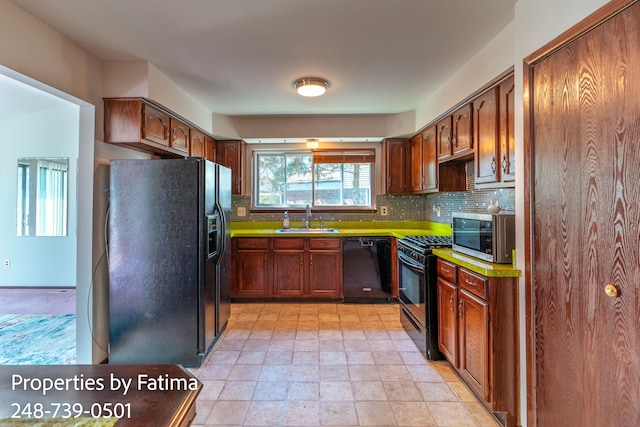 kitchen with a sink, decorative backsplash, black appliances, and stone finish floor