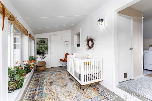 bedroom with wood finished floors, washer / dryer, vaulted ceiling, and a nursery area