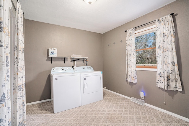 clothes washing area featuring washer and clothes dryer, visible vents, laundry area, and baseboards