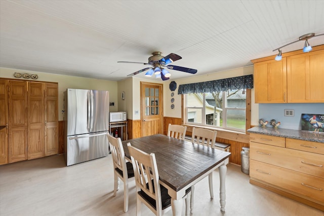dining room with wood walls, ceiling fan, and wainscoting