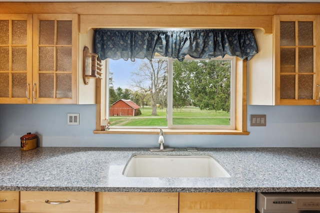 kitchen featuring light brown cabinetry, glass insert cabinets, dishwasher, and a sink